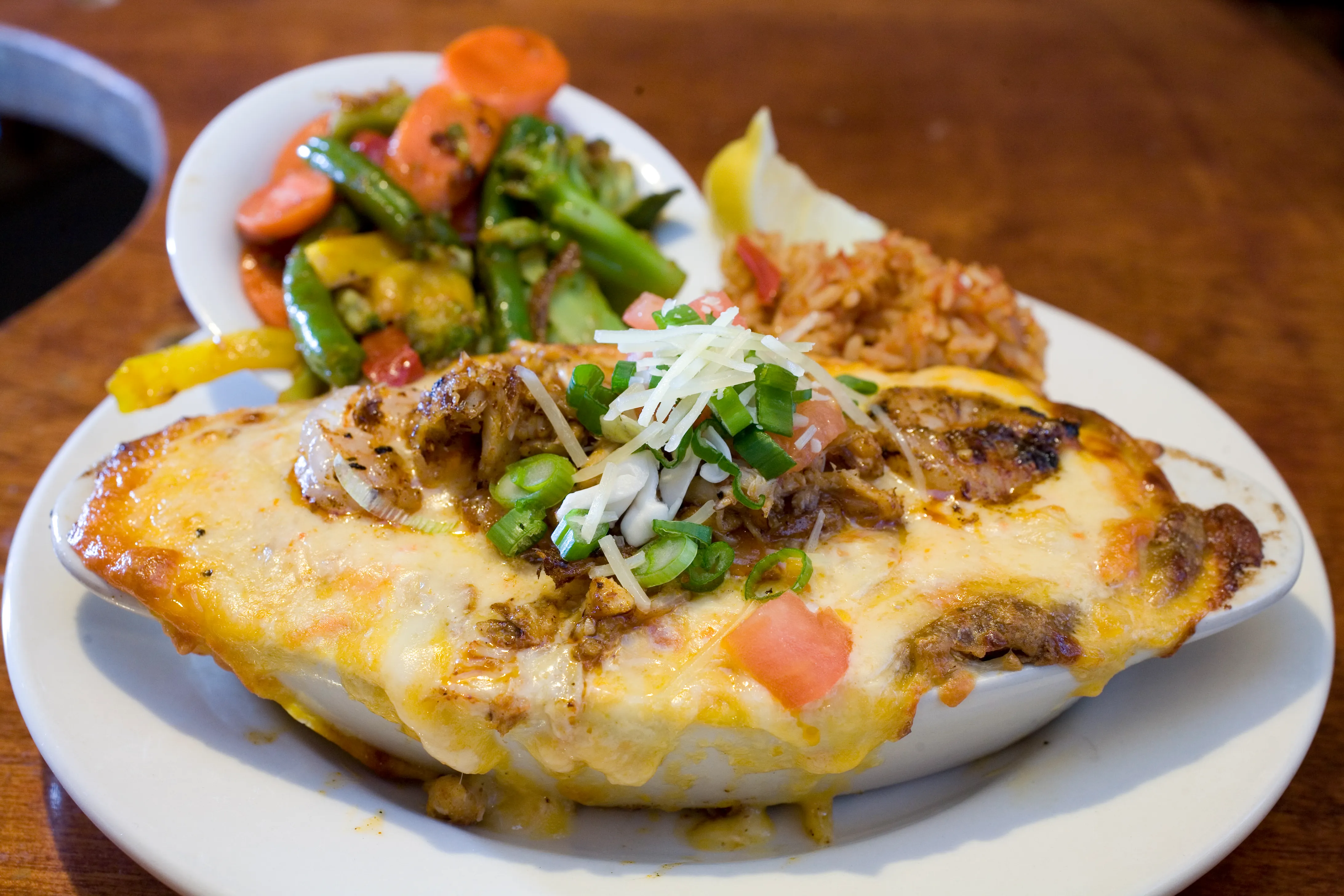 Cheese-baked seafood pot pie topped with scallions, tomato, and parmesan, served with red rice and steamed vegetables.