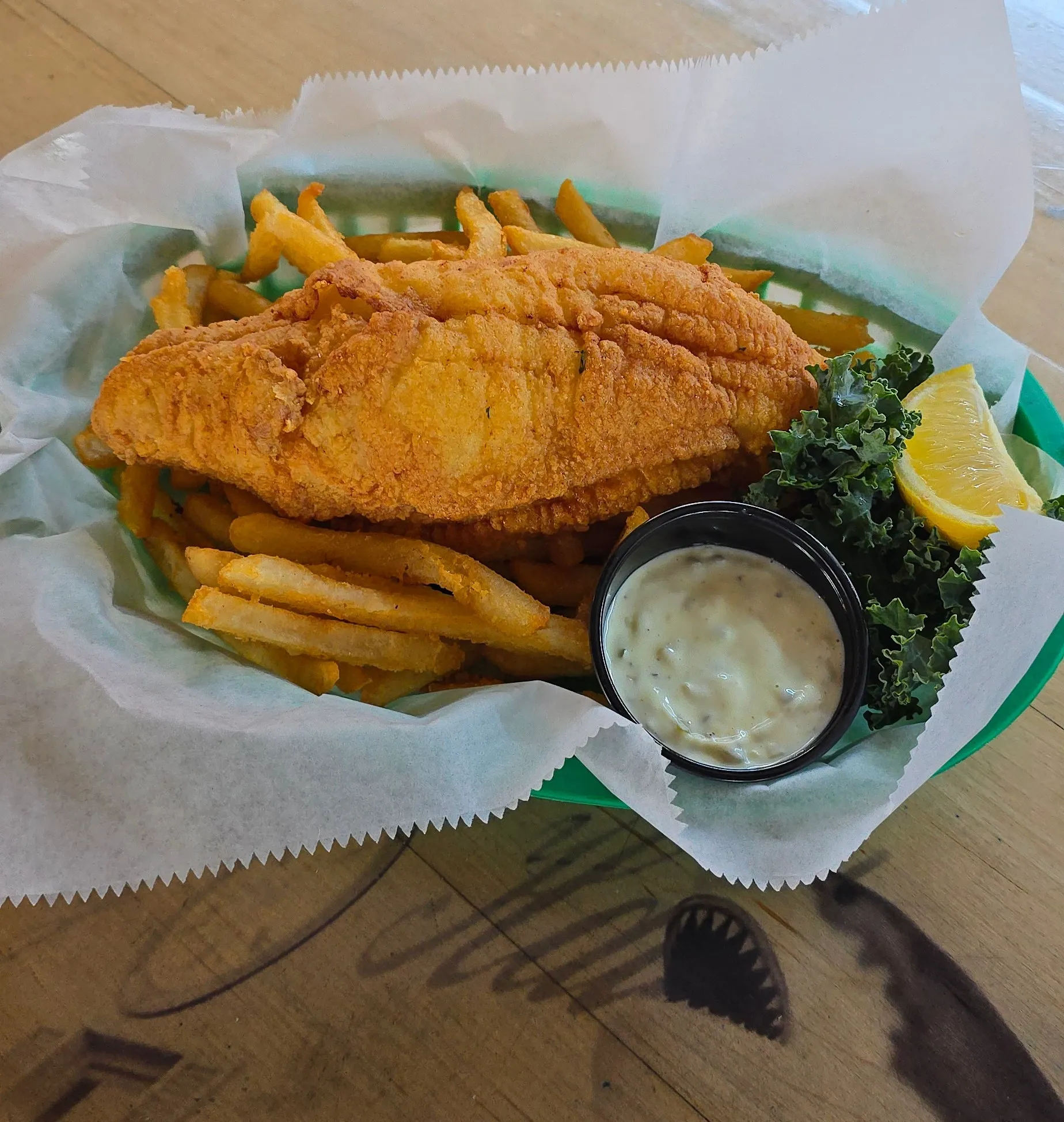 Crispy fried flounder fillet served in a basket with hand-cut fries, tartar sauce, and a fresh lemon wedge.