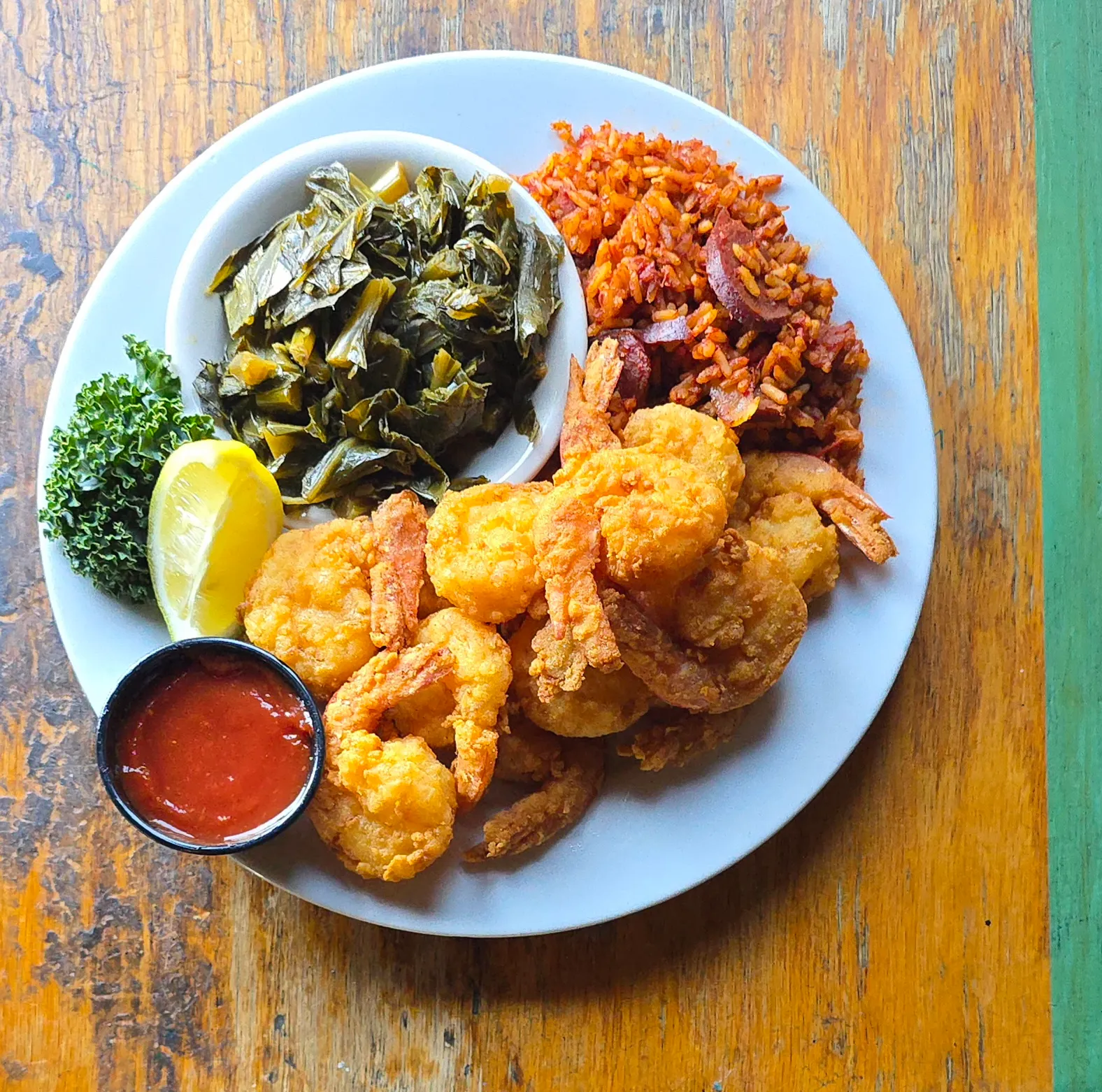 Hand-breaded fried shrimp dinner served with red rice, collard greens, cocktail sauce, and a lemon wedge.
