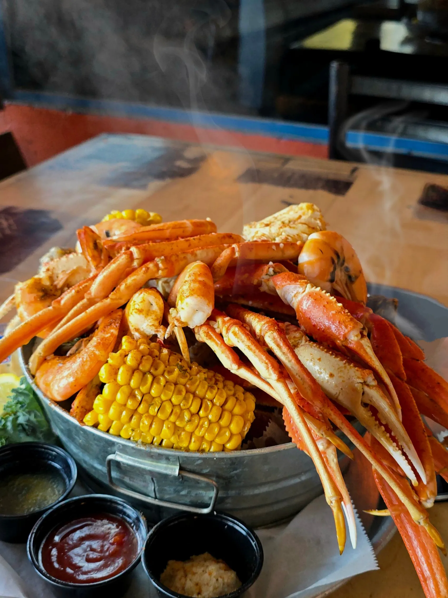 A steaming bucket of snow crab legs, shrimp, and corn on the cob fresh off the steamer, served with drawn butter, cocktail sauce, and horseradish.