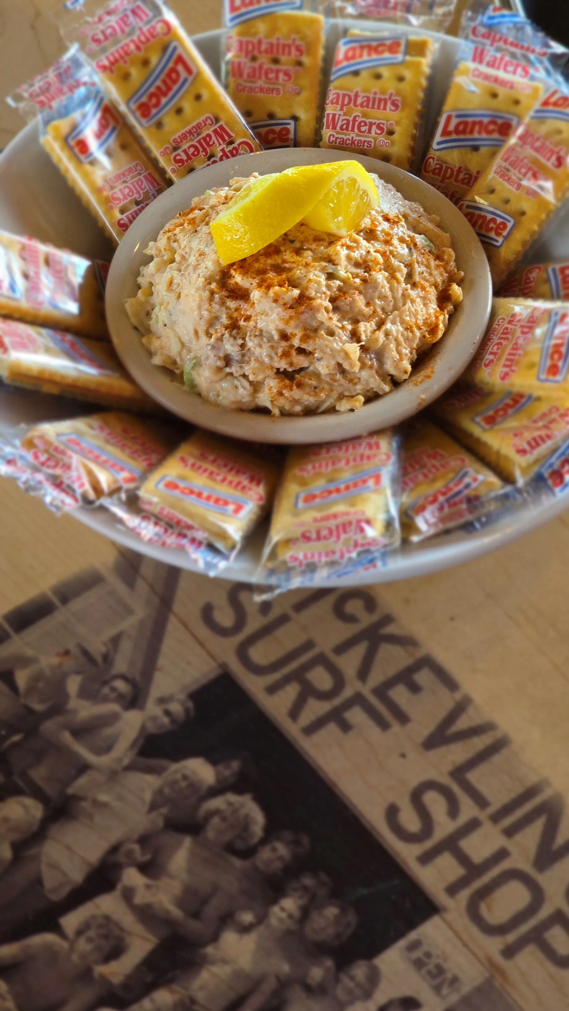 Creamy house-made crab dip dusted with paprika and topped with lemon, surrounded by a fan of Captain's Wafers crackers.