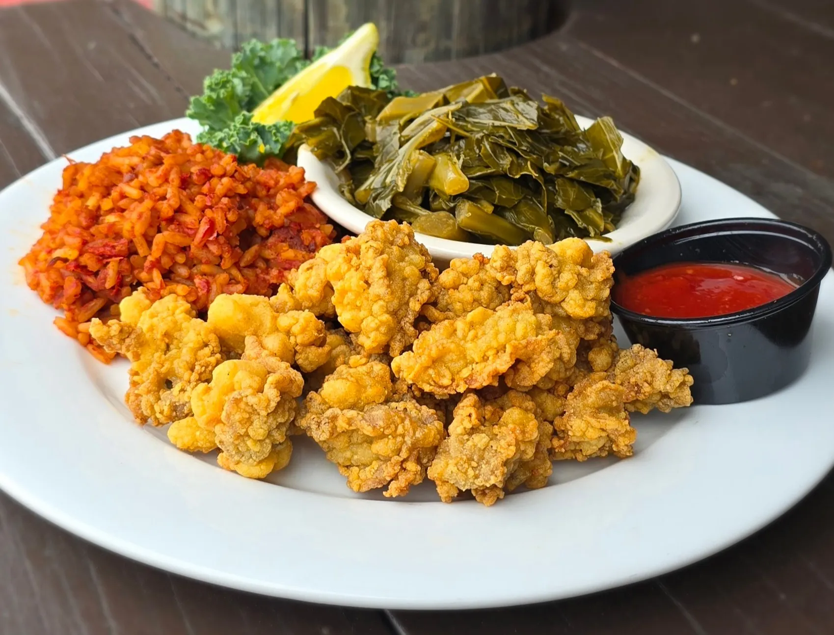 Golden cornmeal-fried oysters plated with red rice, Lowcountry collard greens, cocktail sauce, and a lemon wedge.