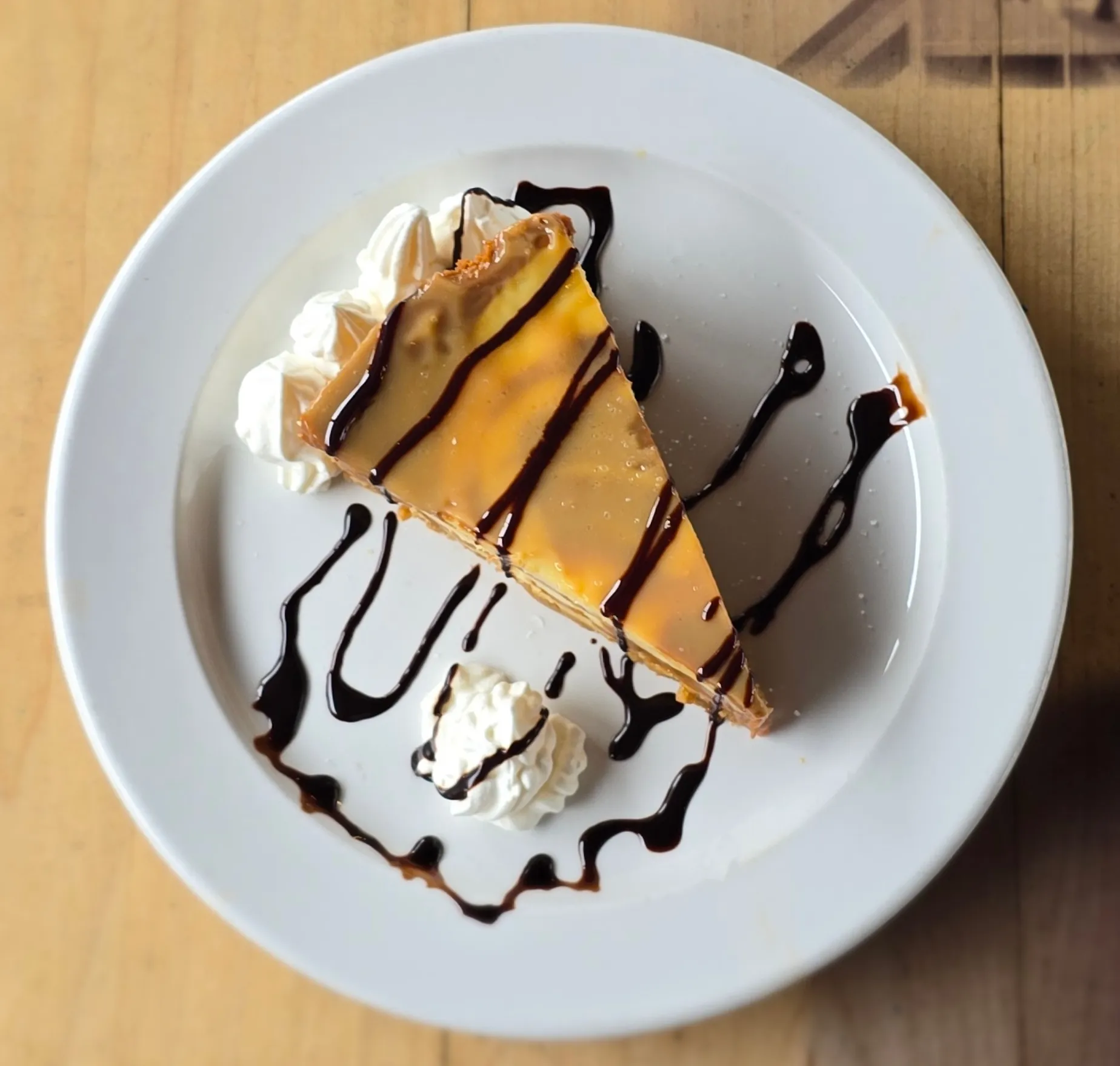 A rich slice of Salted Caramel Pie drizzled with caramel and chocolate sauce, topped with a whipped cream rosette.