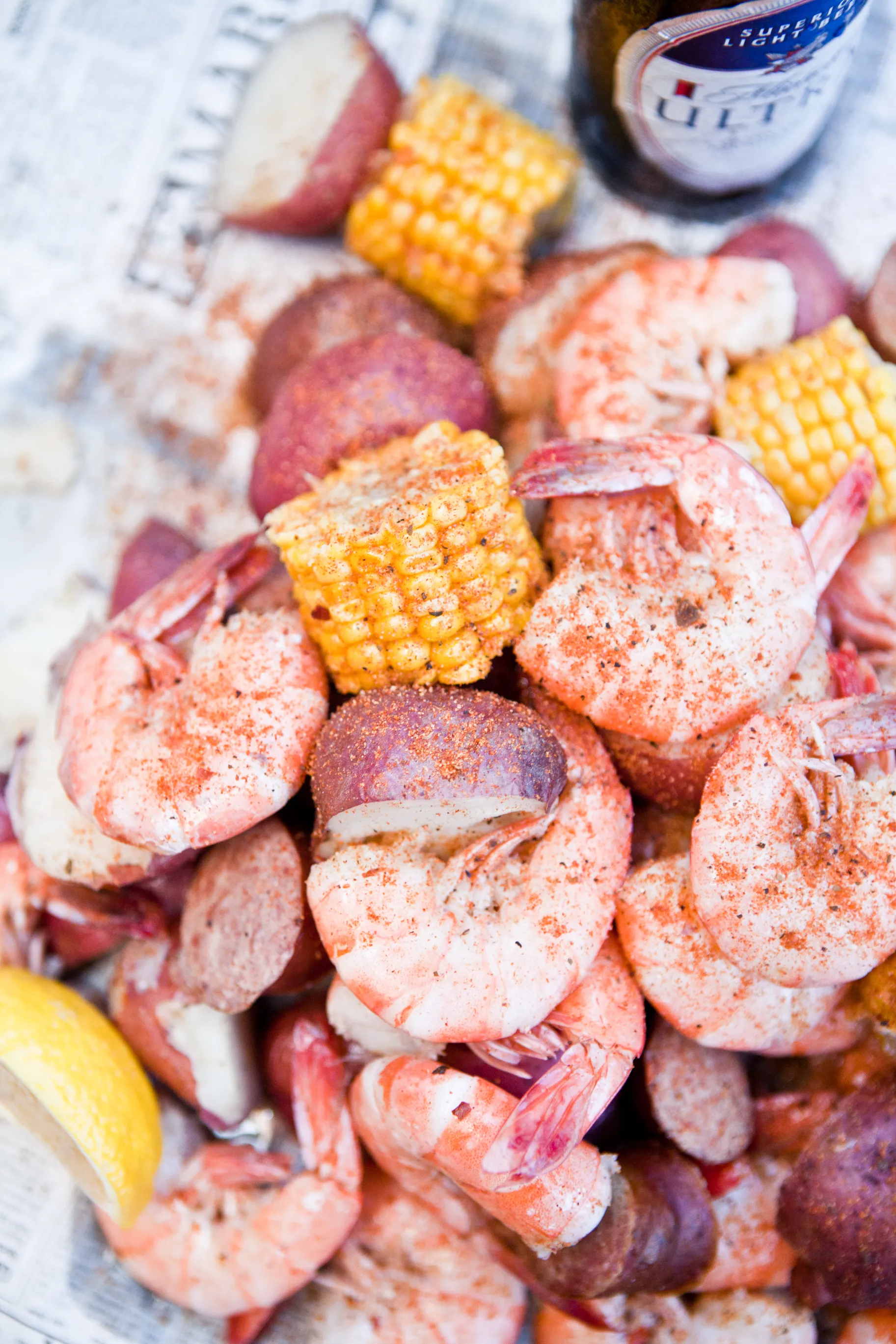 A classic Lowcountry shrimp boil spilled out on newspaper — peel-and-eat shrimp, red potatoes, sausage, and corn on the cob, paired with an ice-cold beer.