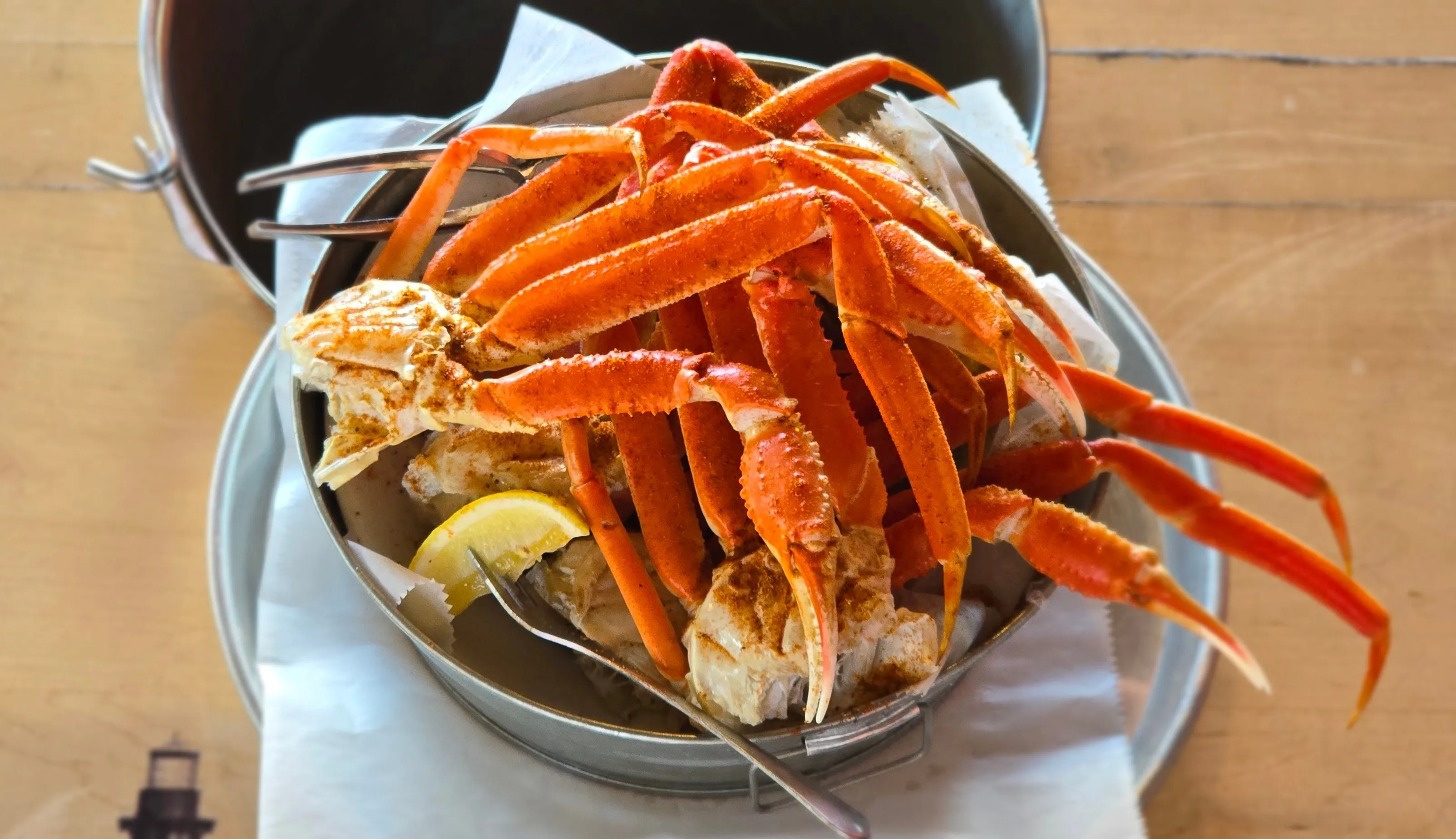 A generous bucket of Old Bay-dusted snow crab legs with a fresh lemon wedge — crackers ready.