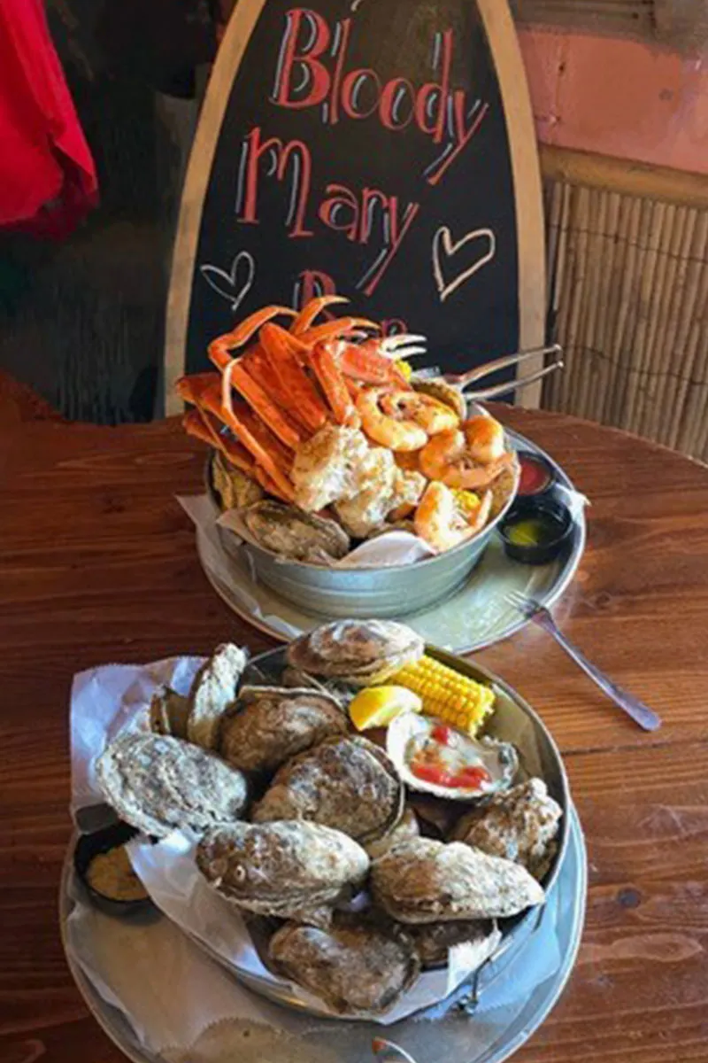 Lively dining room at the Folly Beach Crab Shack — casual no-frills atmosphere featuring overflowing steamed seafood boil buckets with shrimp, crab legs, and Lowcountry sides
