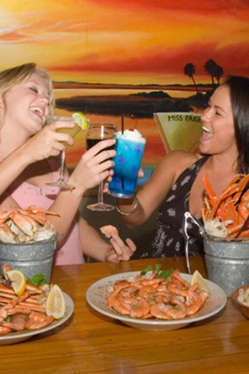 Happy guests enjoying cocktails and cold drinks in the casual coastal dining room at The Crab Shacks — rustic roll-up-your-sleeves seafood atmosphere in Charleston SC